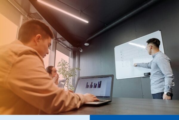 man in professional attire presenting using a whiteboard infront of audience with laptops in office