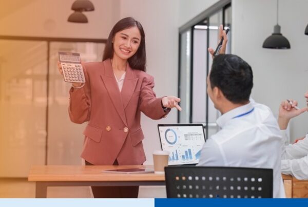 woman in office setting wearing corporate attire presenting while holding a calculator