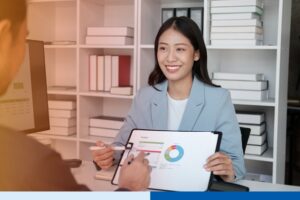 Asian woman in office setting wearing corporate attire smiling while holding report showing data