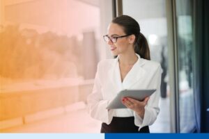 woman in office setting wearing corporate attire smiling while holding a tablet