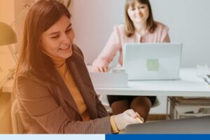 woman with laptop in office setting wearing corporate attire smiling in office