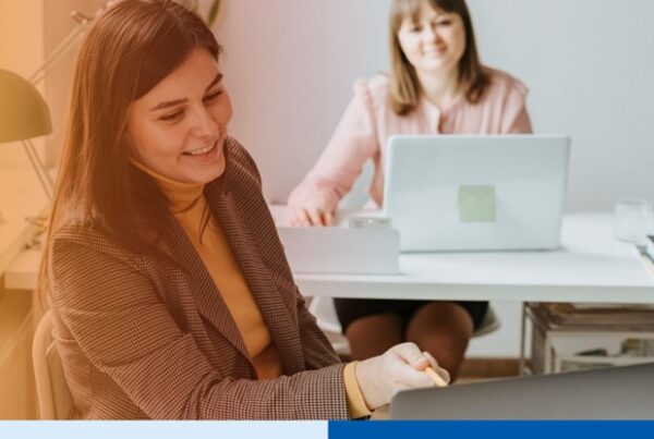 woman with laptop in office setting wearing corporate attire smiling in office