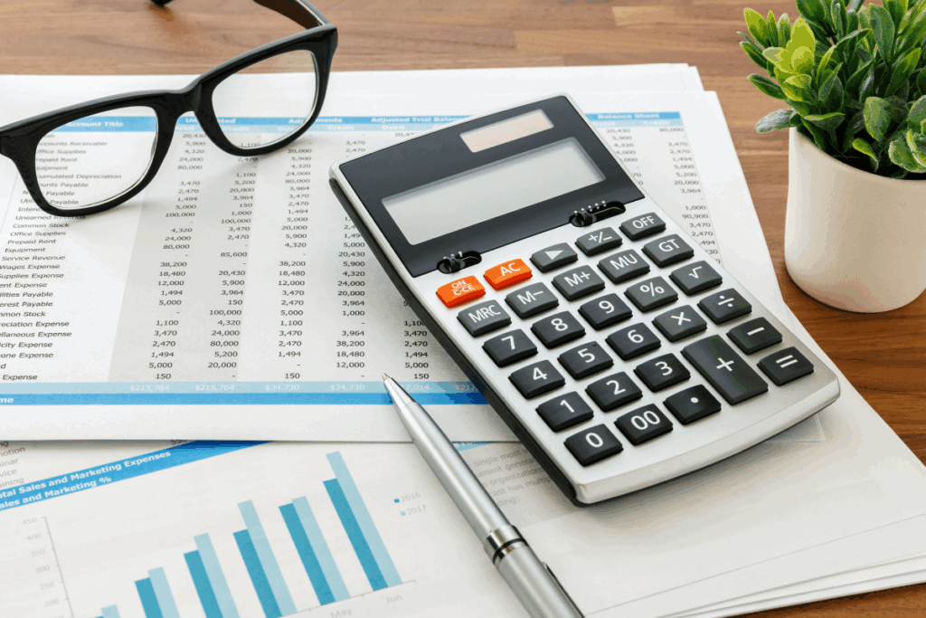 Financial reports, calculator, and glasses on desk representing the detailed accounting work handled by remote bookkeeping companies.
