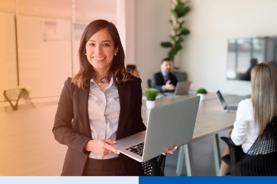 Portrait of smiling female entrepreneur holding a laptop with team in background at office conference room 