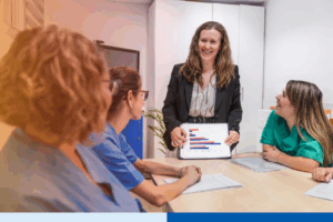 Nurses and a manager discussing data in a nursing home setting, focusing on teamwork and healthcare planning. A tablet displays relevant statistics