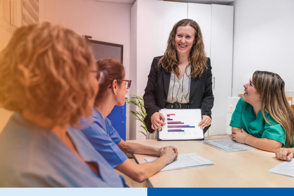 Nurses and a manager discussing data in a nursing home setting, focusing on teamwork and healthcare planning. A tablet displays relevant statistics