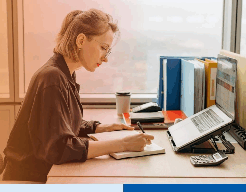 Professional woman working at her desk with a laptop and notebook in a modern office. 
