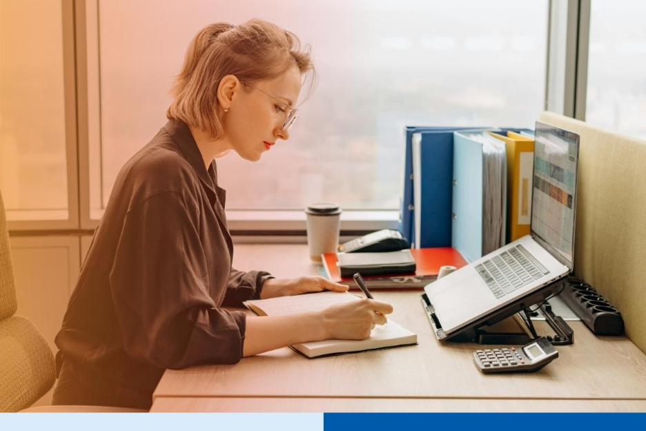 Professional woman working at her desk with a laptop and notebook in a modern office. 