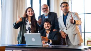 Team of Indian professionals smiling and giving thumbs up while working together at a laptop, representing reliable and collaborative outsourcing support in India.