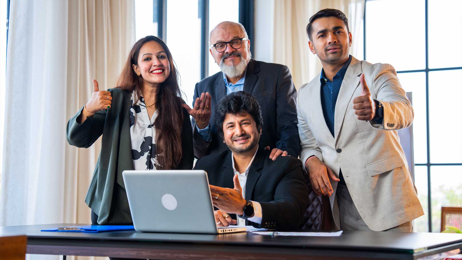 Team of Indian professionals smiling and giving thumbs up while working together at a laptop, representing reliable and collaborative outsourcing support in India.