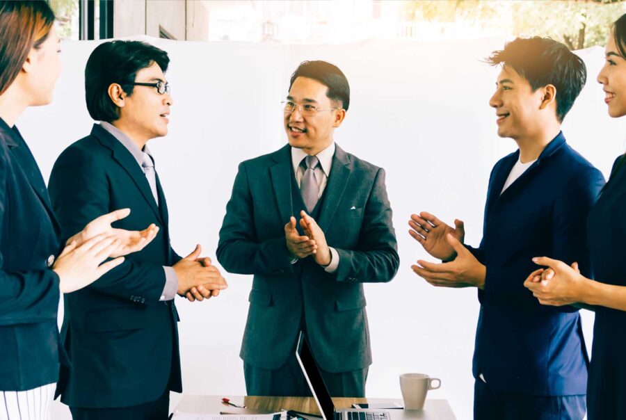 A group of five business professionals engaged in a collaborative discussion around a desk in a bright office setting.