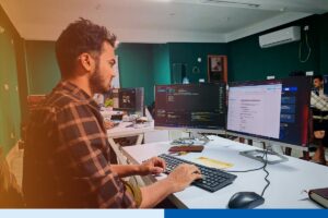 Focused software developer working on code at a dual-monitor workstation in a modern engineering office