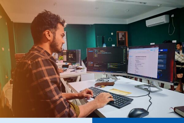Focused software developer working on code at a dual-monitor workstation in a modern engineering office
