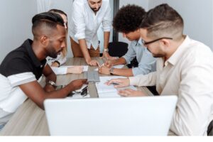 A diverse team of professionals collaborates around a wooden office desk, reviewing data and taking notes, demonstrating agile offshore team management and BPO collaboration solutions.