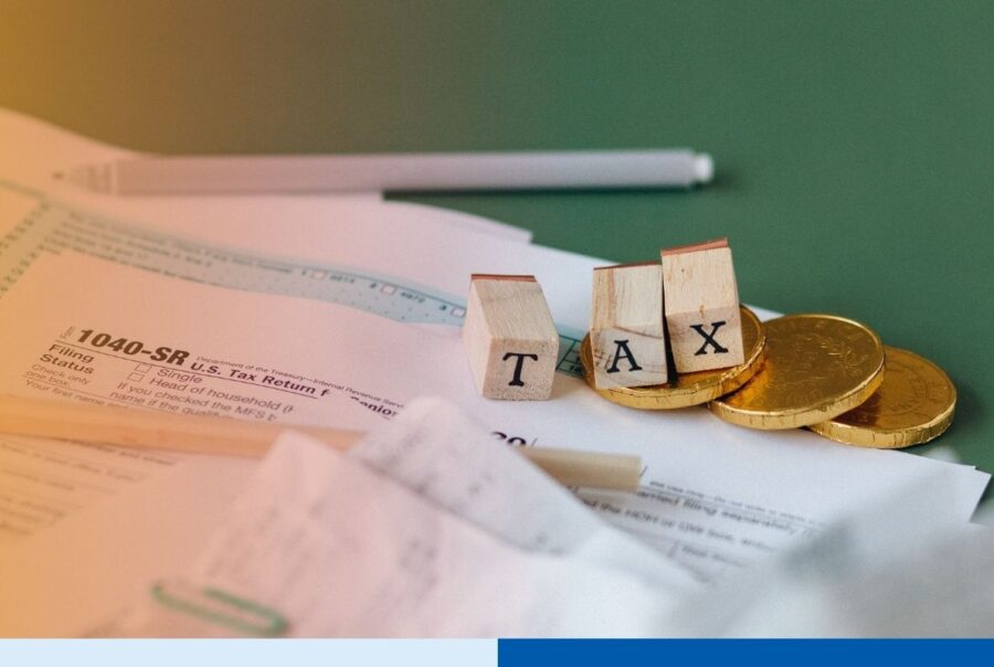 Tax forms, coins, and letter blocks spelling "TAX" on a green desk, representing U.S. tax preparation