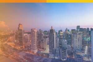 Aerial view of a modern city skyline in the Philippines at dusk, with high-rise buildings, illuminated streets, and a warm sunset glow.