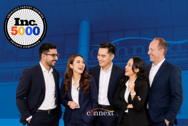 Five Connext Global Solutions professionals standing together in business attire against a blue office background, with the Inc. 5000 badge in the upper left and the Connext logo at the bottom center.