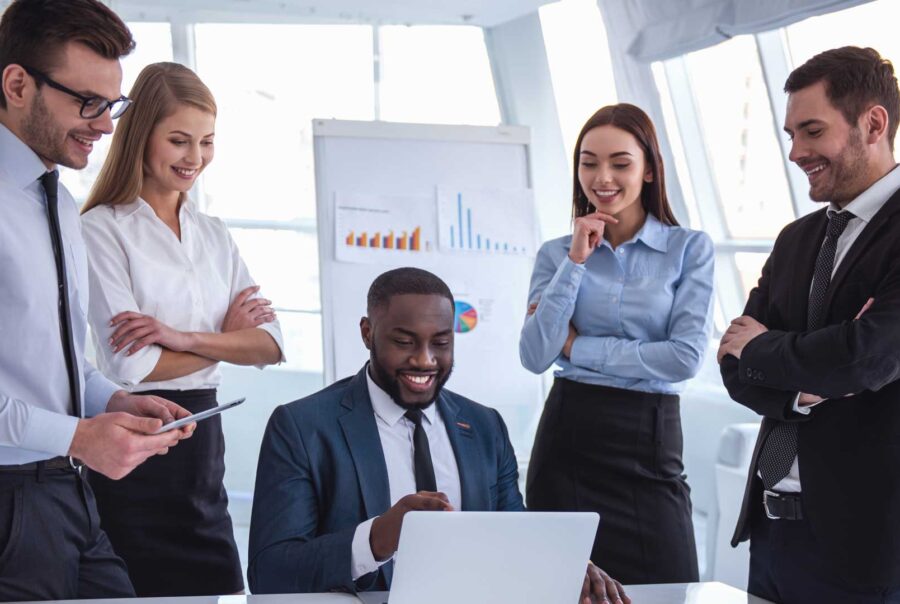 Five business professionals gathered around a laptop in a bright office.