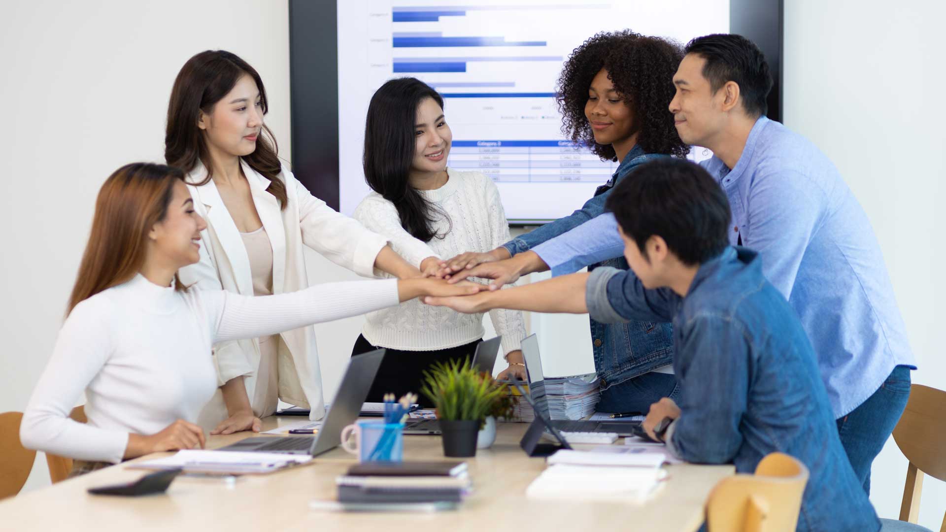 Diverse team members stacking their hands together during a collaborative office meeting.
